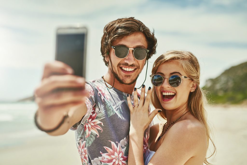 Shot of an affectionate young couple taking selfies after their engagement on the beach